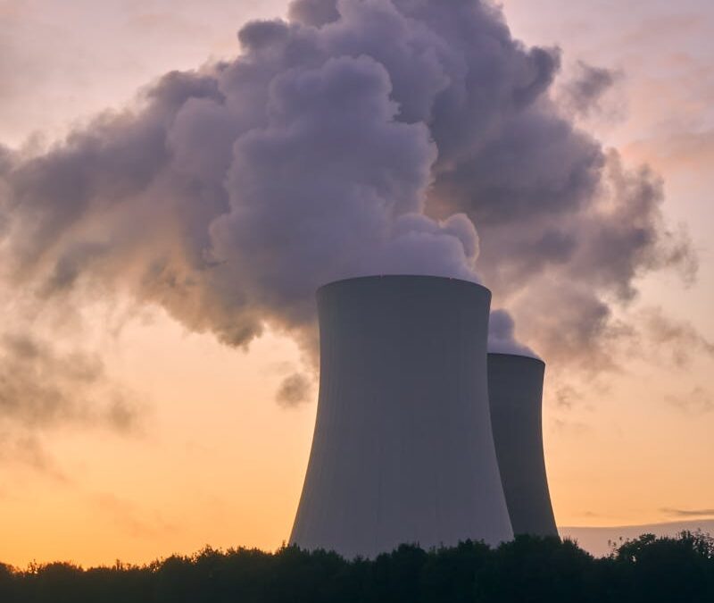 Silhouette of a nuclear power plant emitting steam during a colorful sunset.